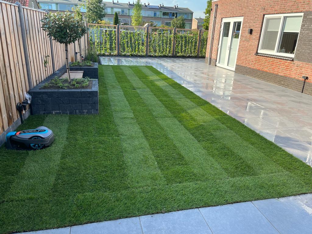 Strak gemaaid gazon met maaistrepen langs een licht terras