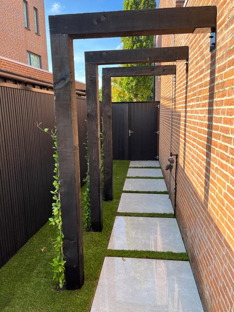 Smal pad langs het huis met zwarte houten klimframes en stapstenen in het gras