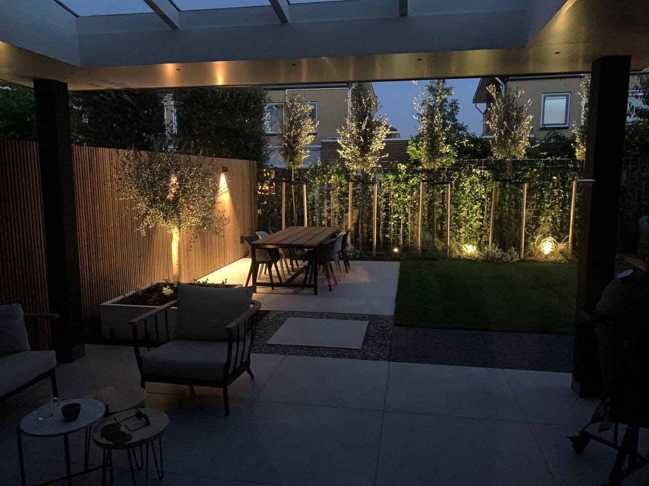 Overkapping bij avond met warme verlichting, loungeset en klimplanten